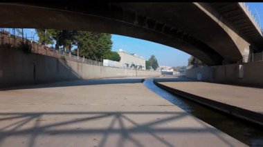 Sakin bir şehir nehir sahnesi bir köprünün altından zarif bir şekilde çekilir, temiz çizgiler ve yumuşak gölgeler vurgulanır. Colfax Caddesi, Los Angeles, Kaliforniya, ABD, Kasım 2024. Yüksek kalite 4k görüntü 