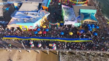 23 Şubat 2025. Ukrayna 'yı desteklemek için Los Angeles, Santa Monica İskelesi' ndeki Pasifik Parkı 'nda barışçıl bir miting düzenlendi. Göstericiler olarak büyük bir Ukrayna bayrağı iskele boyunca uzanıyor.