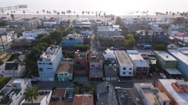 Los Angeles, Kaliforniya 'daki Venice Beach' in insansız hava aracı görüntüleri. Kamera sağdan sola doğru pürüzsüzce hareket ederek renkli evler, uzun palmiye ağaçları ve Pasifik Okyanusu 'nu yakalıyor. Parlak güneş ışığı