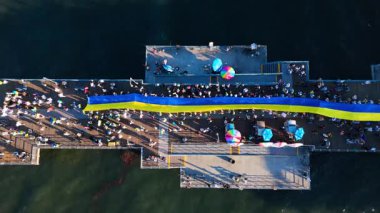 Editör görüntüleri. 23 Şubat 2025. İnsansız hava aracı görüntüleri, Santa Monica İskelesi, Los Angeles, Kaliforniya 'da büyük bir Ukrayna bayrağını çekerken, insanlar destek için toplanıyor. İHA hareket ediyor.