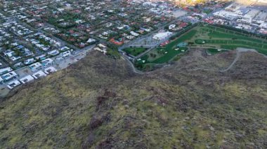 Palm Springs, Kaliforniya 'nın havadan çekilmiş görüntüleri çöl tepeleri boyunca yapılan sinematik iniş yerleşim yerlerini ve güneş doğarken yemyeşil bir golf sahasını gösteriyor. Çarpıcı arazi karşıtlığını gösterirName