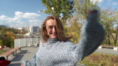 Rahat gri bir kazak giyen neşeli bir kadın güzel manzaralı bir arka planda mutlu bir şekilde poz veriyor. Şehrin çatıları var. Kyiv. Ukrayna, 2021. Ağır çekim. Yüksek kaliteli HD görüntüler