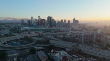 Gündoğumunda Los Angeles şehir merkezinin inanılmaz hava manzarası çarpıcı ışıklandırma ve dağ zeminiyle modern şehir siluetini vurguluyor. Görüntüler şehir mimarisini, yüksek binaları yakalıyor.