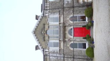 Dikey. Büyüleyici bir video, sarmaşıklarla çevrili canlı kırmızı kapılı görkemli bir taş bina sergiliyor ve çarpıcı mimarisini vurguluyor. Ağır çekim. Yüksek kalite FullHD