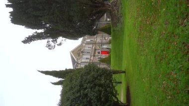 Dikey. Bu sinematik videoda yemyeşil renkli kırmızı kapılı büyük bir ev sergileniyor. Taş bina, doğayla harmanlanmış klasik mimarinin bir örneği. Kilkenny, İrlanda. Yavaş çekim