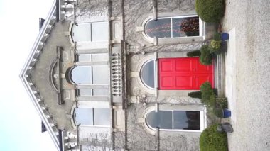 Dikey. Bu video, bir heykelin yanındaki mimari yapının çarpıcı kırmızı kapısının görsel anlatımını inceliyor ve izleyicileri hikayelerini hayal etmeye çağırıyor. İrlanda. Ağır çekim 120 Fp. Yüksek