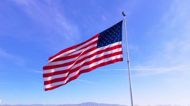 Amerikan bayrağı açık mavi gökyüzüne karşı ağır çekimde zarif bir şekilde dalgalanır, gücü, özgürlüğü ve birliği çağrıştırır. Nefes kesen berraklıkla yakalanan bu vatanseverlik sahnesi ulusal gururu simgeliyor.