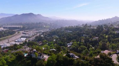 İnsansız hava aracı Los Angeles, Kaliforniya 'daki Universal City yakınlarındaki yemyeşil tepelerin ve yerleşim alanlarının üzerinde süzülüyor. Çerçeve, yumuşak bir sabah sisi altında otoyollar, evler ve yeşillikleri ortaya çıkarır. Nazikçe