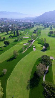 Dikey İHA kamerası ağaçlar, tepeler ve uzak dağlarla çevrili geniş bir golf sahası üzerinde sabit bir şekilde ilerler. Sabah sisi manzaraya derinlik ve yumuşaklık katar. Manikürlü