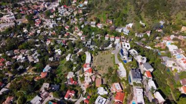 Dinamik 4K hava görüntüleri Los Angeles, Kaliforniya 'daki Hollywood Hills yakınlarında manzaralı bir yerleşim yeri olduğunu gösteriyor. İnsansız hava aracı yamaçtaki evlerin, dolambaçlı sokakların ve yemyeşil sokakların üzerinde sorunsuzca uçuyor.