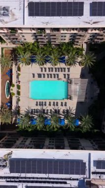 Dikey İHA görüntüleri, Los Angeles 'taki lüks bir yerleşim yerinde palmiye ağaçları, kabinler ve şezlonglarla çevrili modern bir yüzme havuzunun tepeden tırnağa görüntüsünü gösteriyor. Kamera yavaşça hareket ediyor.
