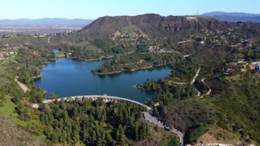 Hollywood Gölü 'nün çarpıcı hava manzarası ve Santa Monica Dağları' ndaki ikonik Hollywood tabelası. İHA görüntüleri su deposunda, yemyeşil alanda ve dolambaçlı yollarda net yansımalar yakalar.