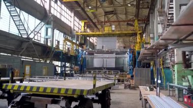 Endüstriyel üretim salonunun geniş açısında vinçler, mekanik ekipmanlar, çelik taşıma hatları ve sarı-siyah güvenlik platformları var. Boşluk merdiven, kontrol panelleri ve