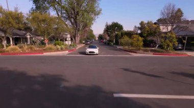 Los Angeles, Kaliforniya, ABD 'deki manzaralı bir yerleşim yerinden geçen beyaz bir arabanın görüntüsü. Kamera yükselirken geriye doğru sorunsuzca hareket eder ve sinematik bir görüntü sağlar.
