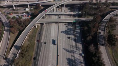Los Angeles, Kaliforniya 'daki karmaşık bir otoyol kavşağının nefes kesici yavaş çekim hava görüntüsü. Kamera, çeşitli üst geçitler ve yollar boyunca ilerleyen araçları yakalıyor.