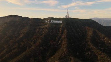 Los Angeles tepelerindeki ünlü Hollywood tabelasına yaklaşan insansız hava aracı görüntüleri. Kamera ileriye doğru uçuyor, engebeli araziyi ve efsanevi beyaz harfleri yakalıyor.