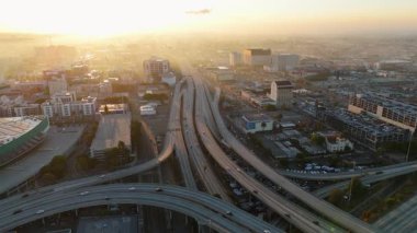 Los Angeles, Kaliforniya 'da 24 Ekim 2024' te gün doğumunda çekilmiş çok katlı bir otoyol kavşağının insansız hava aracı görüntüleri. Araçlar, yumuşak altın ışık altında kıvrımlı otoyollar boyunca ilerler.