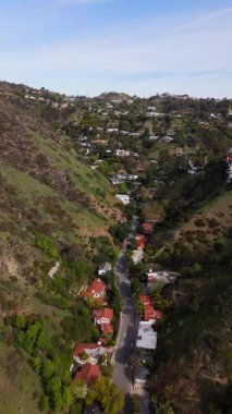Los Angeles California 'nın Hollywood Tepeleri' ndeki lüks konutların üzerinde ilerleyen insansız hava aracı görüntüleri. Yeşil yamaçlar ve manzaralı yollarla çevrili bu elit yamaç arazileri sergileniyor.
