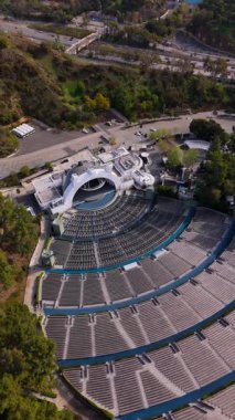 Los Angeles 'taki Hollywood Bowl Amfitiyatrosunun dikey insansız hava aracı çekimi. Eğimli koltuklar, sahne ve etrafındaki ağaçlar ve tepeler. İkonik mimariyi, kültürel mekanı ve manzarayı yakalar