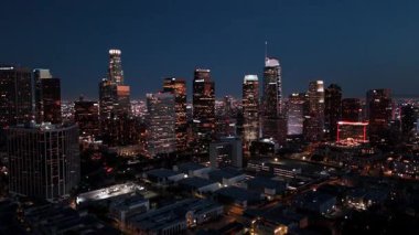 14 Nisan 2025 'te Los Angeles şehir merkezinin aydınlık siluetinden çekilen sinematik ters hava aracı çekimi. Çerçeve ikonik gökdelenlerin alacakaranlık gökyüzüne karşı parladığını gösteriyor.