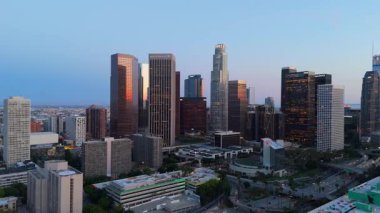 Alacakaranlıkta Los Angeles şehir merkezinin sinematik hava manzarası, insansız hava aracı aydınlık gökdelenler ve işlek şehir caddelerinde yavaşça soldan sağa dönüyor. Altın akşam parıltısı
