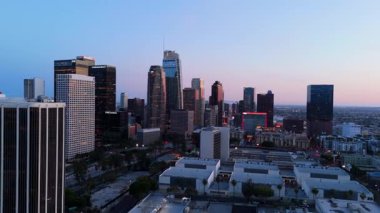 11 Nisan 2025 'te Los Angeles şehir merkezinin hava görüntüsü sağa doğru hareket ediyor. Aydınlatılmış gökdelenler ve City National Bank ve TCW gibi görünen şirket logoları,