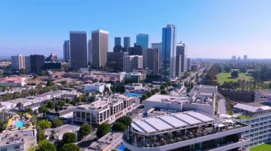 Beverly Hills üzerinde ileri hareket çekimi Los Angeles şehir merkezinin panoramik manzarasını ve modern cam gökdelenleri gözler önüne seriyor. Wilshire ile ön planda beyaz bir çatı restoranı görülebiliyor.