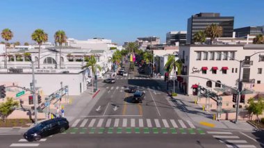 Beverly Hills, Los Angeles 'taki Rodeo Drive ve Brighton Yolu' nun kesiştiği yerde ileri doğru yumuşak bir dron atışı var. Çerçeve, palmiye çizgili sokakların üzerinde zahmetsizce süzülüyor.
