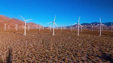 İHA görüntüleri, sabahın erken saatlerinde ufka doğru uzanan büyük bir rüzgar türbini çiftliğinin geniş bir görüntüsünü yakalıyor. Sahnede bir kuraklığa karşı yenilenebilir enerji altyapısı sergileniyor
