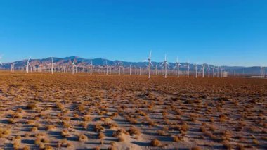 Güneşin doğuşunda bir rüzgar çiftliğinin havası, kamera yavaşça yükselirken çölden ufka doğru uzanan büyük bir türbin alanını ortaya çıkarıyor. Beyaz yel değirmenleri dimdik ayakta