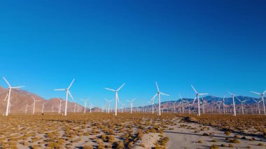 Kamera, Palm Springs 'in çöl dağlarına kurulmuş uçsuz bucaksız bir rüzgar çiftliğinden geçiyor. Parlak güneş ışığı ve açık gökyüzü temiz enerji manzarasını vurgular. Sürdürülebilirlik temaları için ideal
