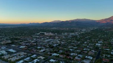 Palm Springs, Kaliforniya 'nın hava görüntüsü, 14 Nisan 2025' te gündoğumunda çekildi. İnsansız hava aracı geriye doğru uçuyor ve dramatik dağ siluetleri tarafından çerçevelenmiş yerleşim yerlerini yavaş yavaş ortaya çıkarıyor. Şey...