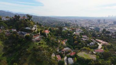 Los Angeles California 'nın Hollywood Tepeleri' ndeki lüks evlerin üzerinde ilerleyen insansız hava aracı görüntüleri. Yeşillik ve şehir manzaralarıyla çevrelenmiş bu özel mülkler lüks yaşamı ön plana çıkarıyor.