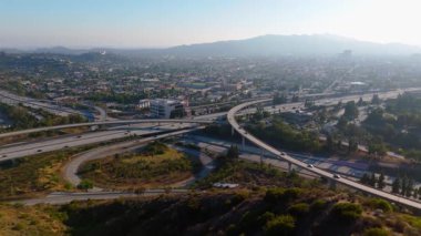 Los Angeles, Kaliforniya 'da genişleyen bir otoyol kavşağının havadan görünüşü katmanlı üstgeçitlerle ve şehrin ufuk çizgisine doğru uzanan eğrilerle. Kamera otoyolun üzerinde uçuyor.