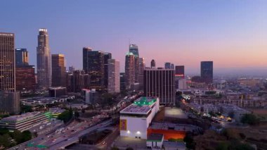 Günbatımında Los Angeles şehir merkezinin insansız hava aracı görüntüsü modern gökdelenleri, Bank of America kulesini ve kalabalık 110 otobanı yakalıyor. Sıcak akşam ışığı vurguluyor