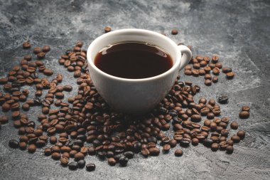 Kahverengi kahve çekirdekleri ve koyu yüzey desenli tahıl grubu üzerinde bir fincan kahve.