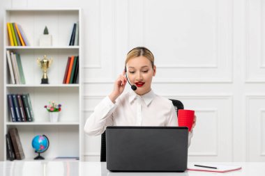 Müşteri hizmetleri şirin sarışın ofis gömleği, kulaklık ve bilgisayarla bir müşteriyle konuşuyor.