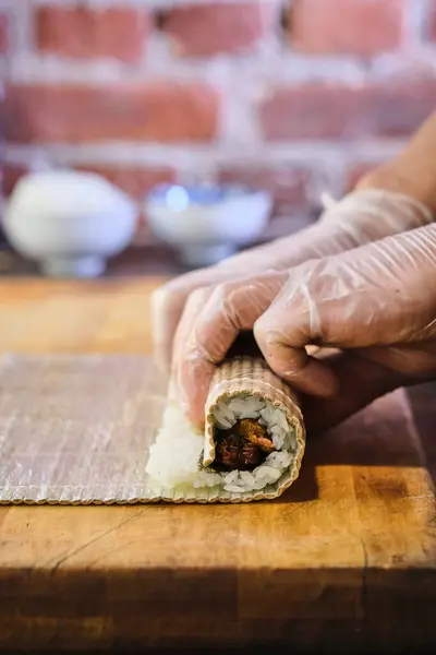 stock image A culinary artist skillfully rolls sushi, blending savory stuffed ingredients with seasoned rice, all set against a warm, inviting kitchen backdrop.