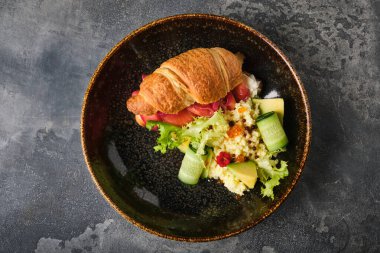 Lezzetli somon kruvasan sandviçi, süslenmiş ve sade, dokulu bir tabakta sunuluyor, lezzet ve dokuların karışımı sunuluyor..