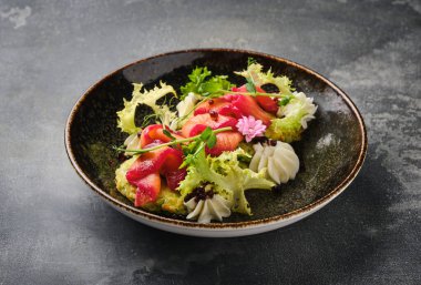 Canlı bir görüntü, taze otlar ve yenilebilir çiçeklerle süslenmiş, koyu dokulu bir yüzeyde, kırsal bir kasede servis edilen güzel bir somon salatası sergiliyor..