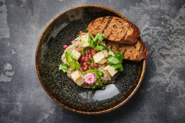 Lezzetli bir gurme tofu salatası, taze otlarla süslenmiş ve yanında da klas bir kasede sunulan ızgara ekmek..
