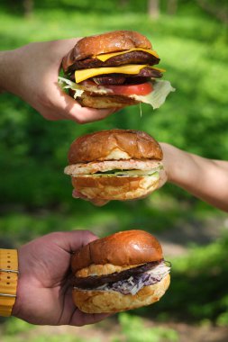 Üç arkadaş bereketli yeşilliklerle çevrili gurme burgerlerini güneşin altında neşeyle sergiliyorlar. Her hamburger eşsiz malzemeler ve dolgularla övünür. Birlikte lezzetli bir yemek sözü verir..