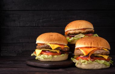 Three delicious cheeseburgers are artfully arranged, showcasing layers of melted cheese, vibrant vegetables, and savory sauces, inviting a delightful culinary experience. clipart