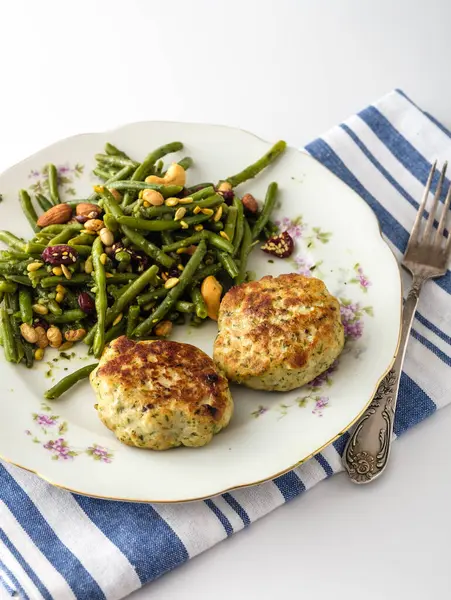 stock image A vibrant plate showcases two golden fish cakes and a fresh green bean salad topped with nuts, capturing a delightful culinary experience in a charming setting.