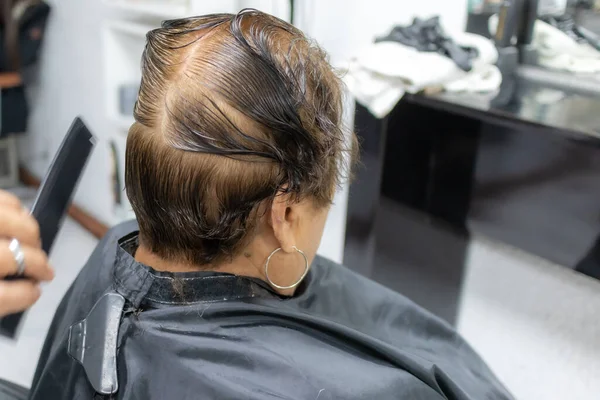 Rear view of wet hair with a line in middle of head on a blurred background, stylist cutting an elderly woman\'s hair, brown dye, beauty salon procedure. Concept of beauty in the elderly