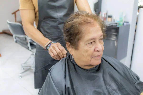 Old woman in beauty salon, sitting on a chair before getting her hair cut against a blurred background, brown tint, beauty salon procedure. Concept of beauty in the elderly