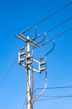 Yüksek voltajlı elektrik direğinin tepesi, elektrik kabloları, arka planda açık mavi gökyüzü olan güneşli bir gün, daha düşük bir perspektiften görülüyor.