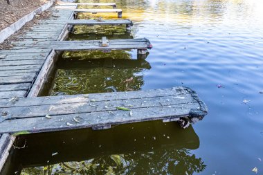 Platformları olan eski ahşap yürüme platformları halka açık bir parkta küçük bir rıhtımda tekneler demirliyor, Meksika 'da güneşli bir kış günü, su yüzeyinde ışık yansıması.