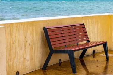 Boş ahşap bank, deniz suyuyla ıslanmış, sahil kıyısında bir çitin yanında, arka planda deniz, dalgasız mavi su, La Paz, Baja California Sur Mexico 'da sakin ve bulutlu bir gün.