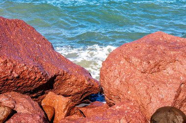 Deniz ile kırmızımsı kahverengi kayalar ve arka planda küçük dalgalar, kayalık kıyı şeridi, suya yansıyan güneş ışığı, Baja California Sur Mexico 'da güneşli bir gün